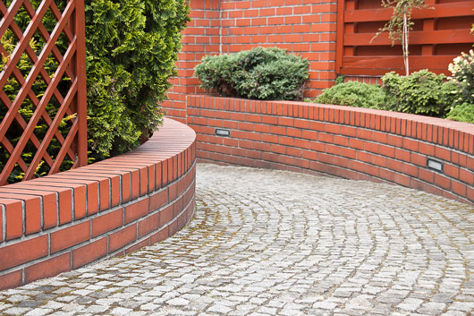 curved brick wall in a garden surrounded by greenery with cobblestone pathway balancing aesthetics and functionality for landscape design 5 landscaping ideas