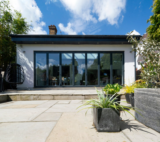 modern home exterior with large glass doors surrounded by planters showcasing five vibrant plants and a clear blue sky