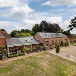aerial view of a charming brick house with a patio area surrounded by greenery and a gravel pathway showcasing outdoor seating perfect for gatherings and two relaxing spaces