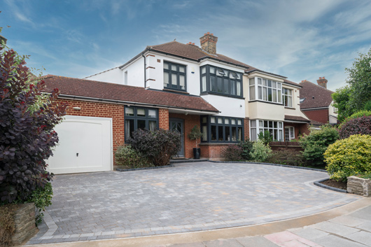 two story brick house with a paved driveway and landscaped garden surrounded by green shrubs and trees