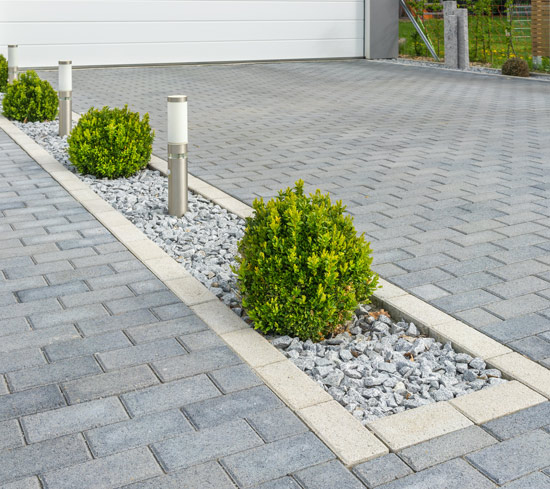 landscaped driveway with two green bushes illuminated by modern lamps featuring gray paving stones and decorative gravel