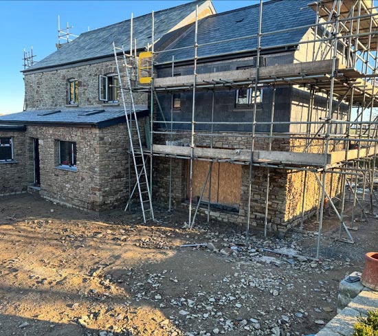 construction site of a stone house with scaffolding and building materials showcasing progress on the new home project